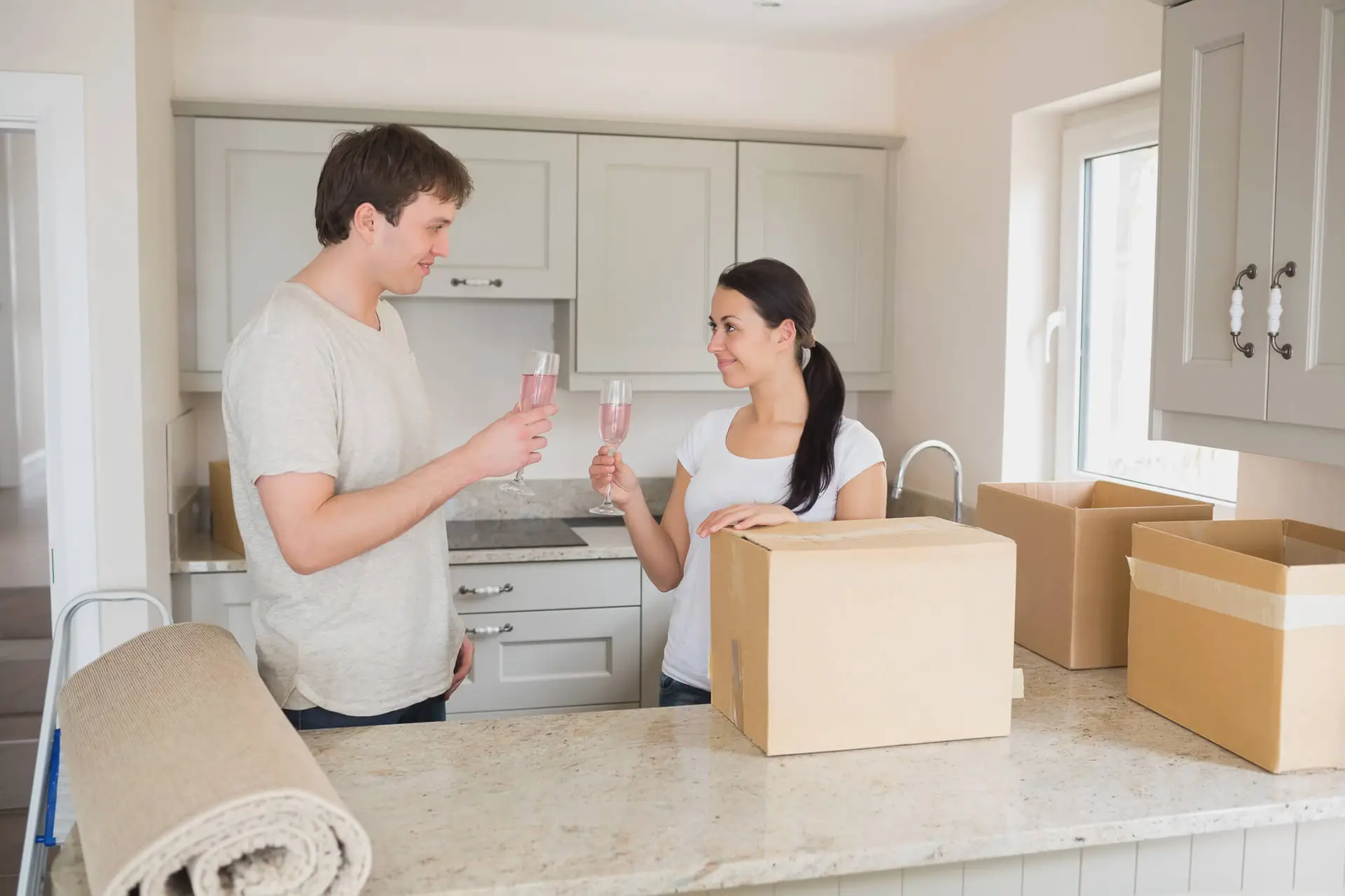 Happy couple toasting with champagne glasses in their new home kitchen surrounded by moving boxes