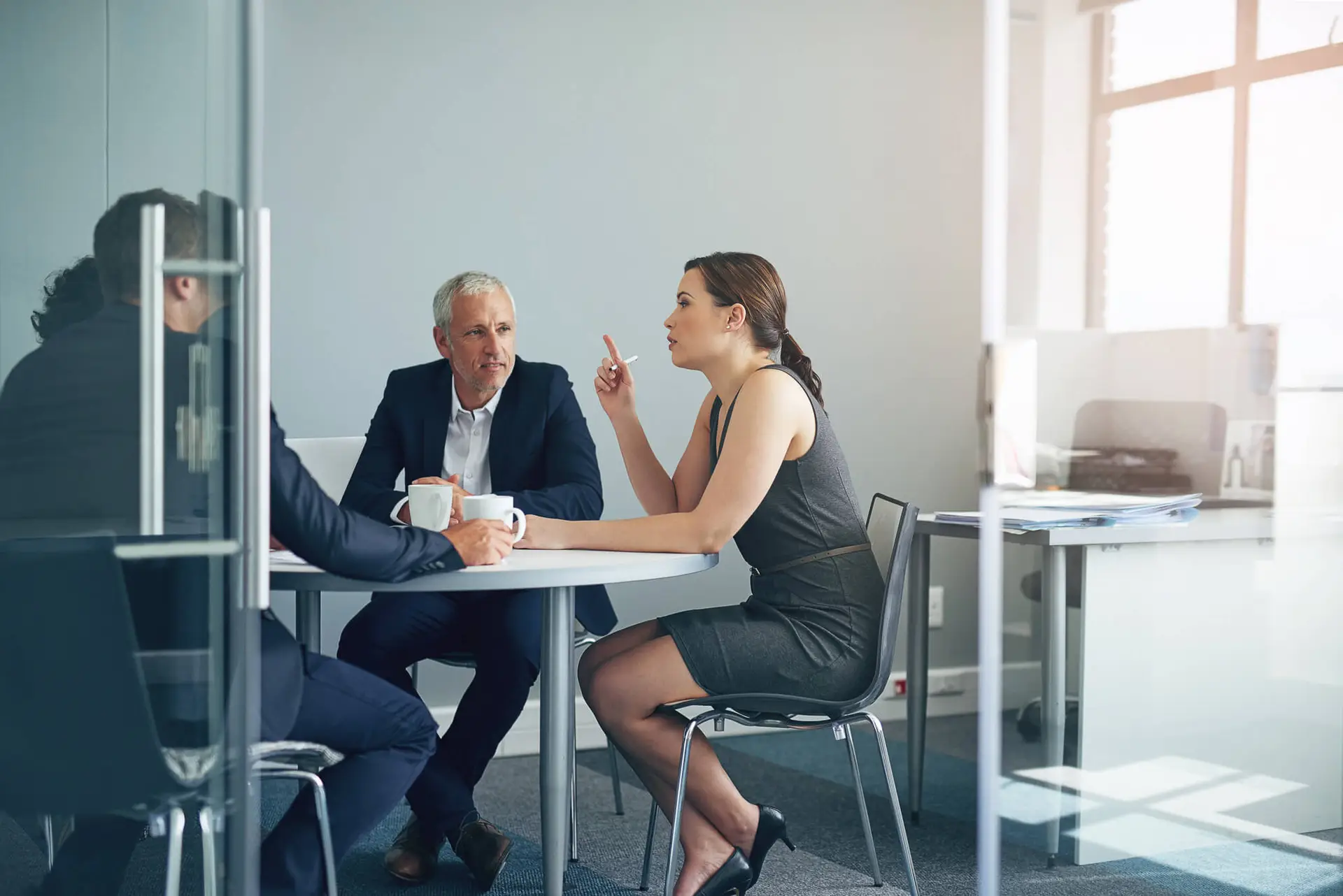 Two professionals having a business discussion at a table in a modern glass-walled office