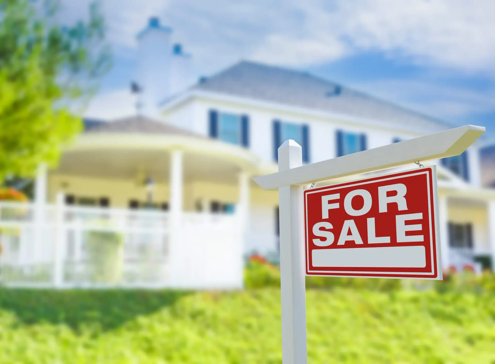Red and white "For Sale" sign in front of large two-story house with porch and green lawn.