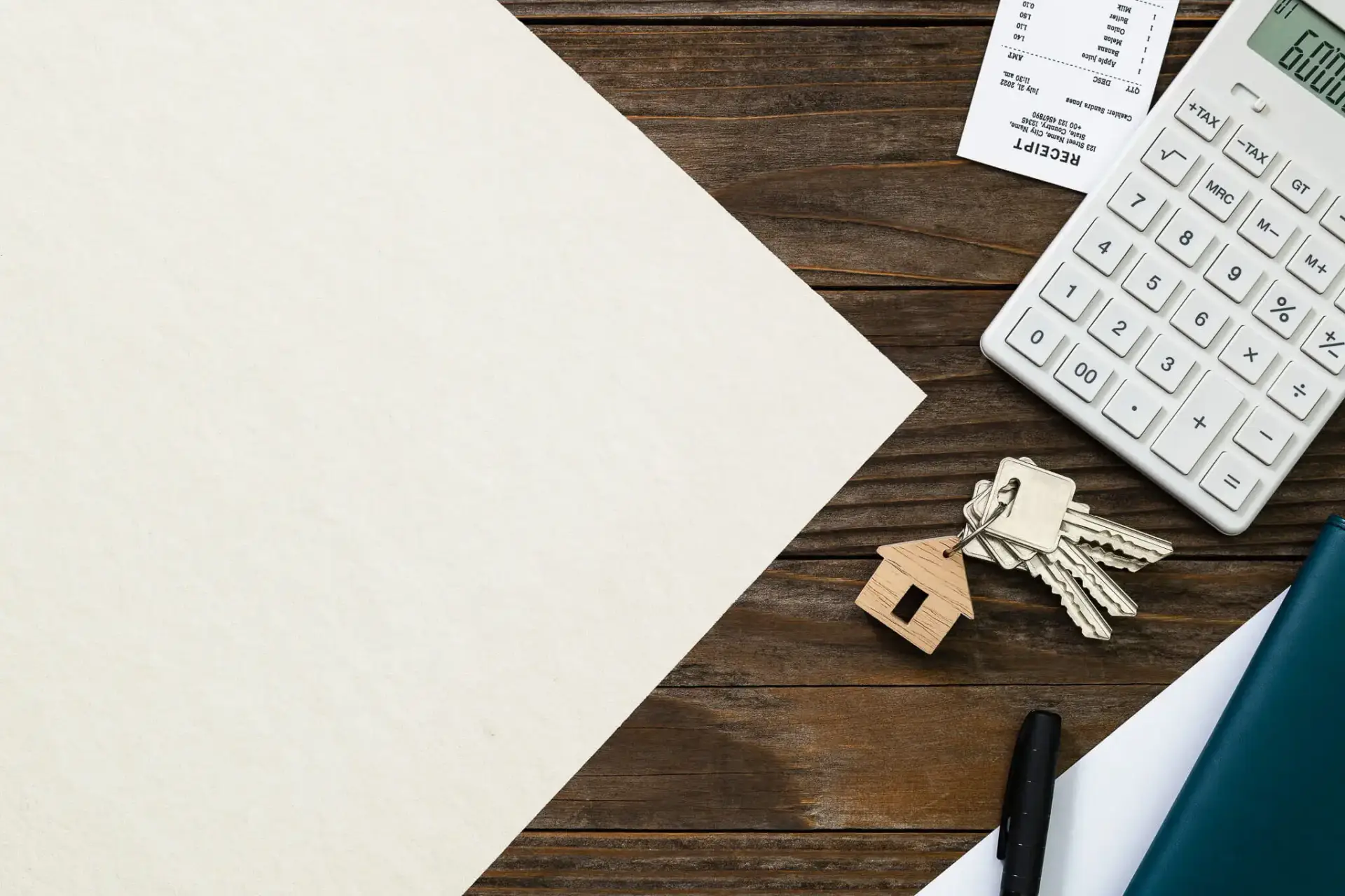 A calculator, receipt, pen, keys with a house-shaped keychain, and blank paper lie on a wooden desk.