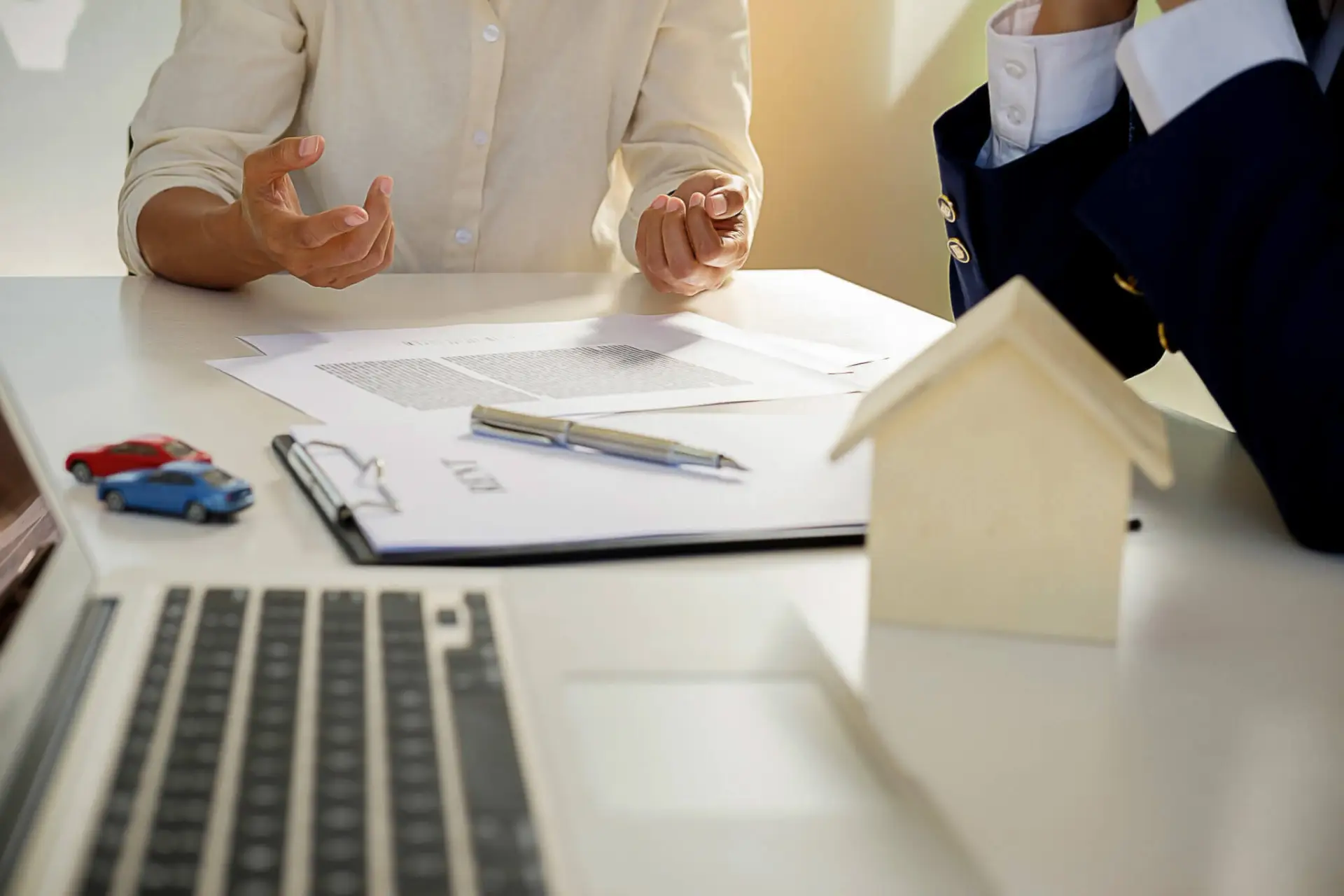 Sebastian Skibinski Two people are sitting at a desk with documents, a pen, small car models, and a house model, suggesting a discussion about real estate or car insurance. Mortgage Agent
